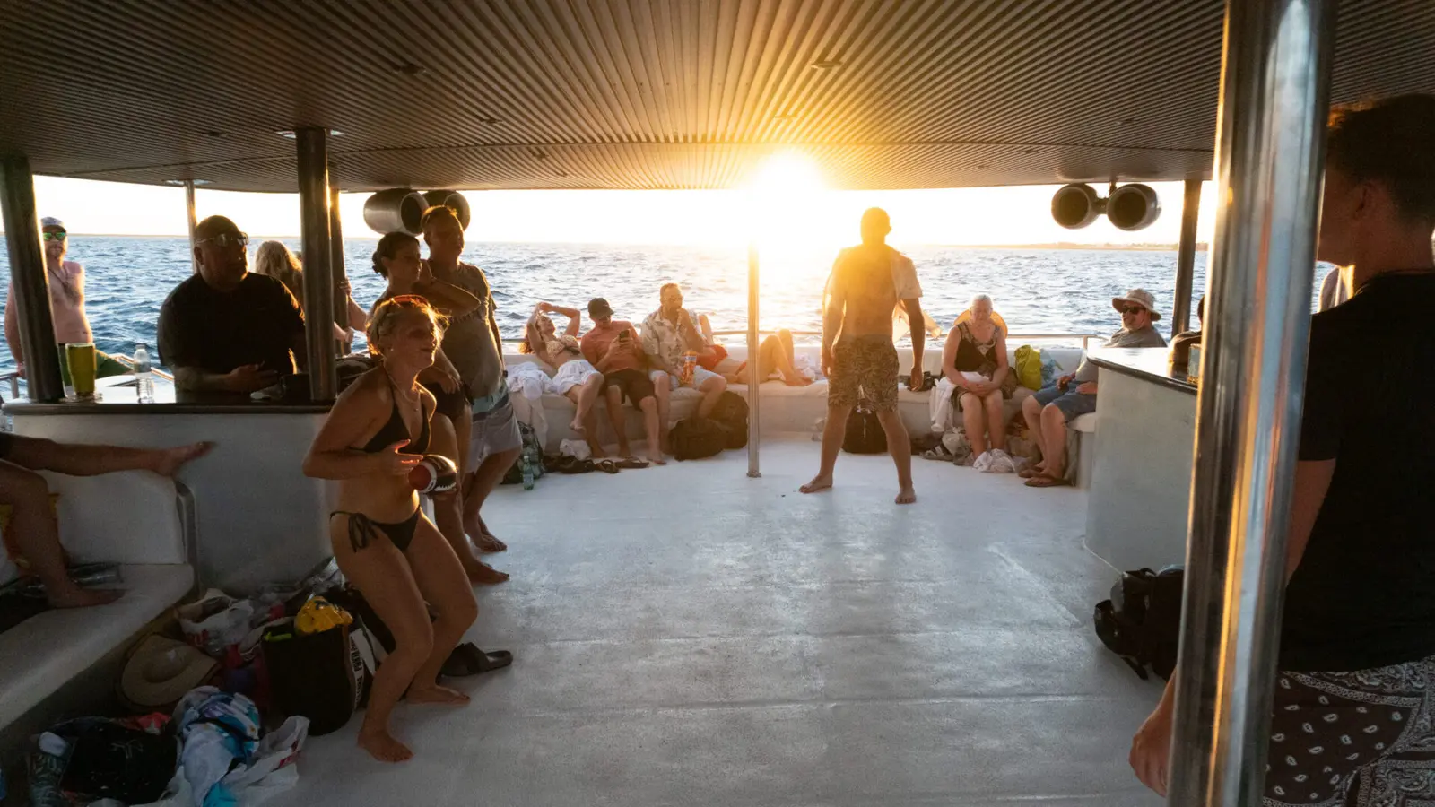 Guests dancing and lounging on the catamaran's covered deck as the sun sets over the sea