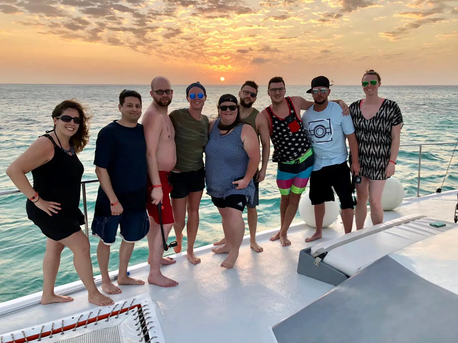 Group of guests posing on a catamaran deck under a golden sunset sky off Aruba