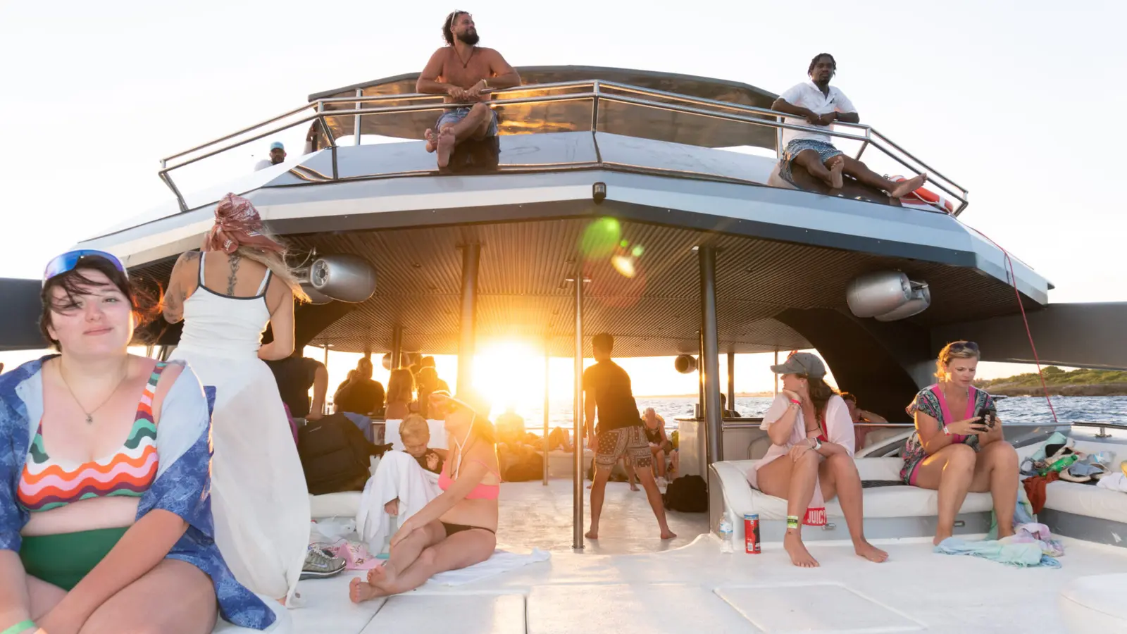 Guests relaxing on the catamaran's deck as the sun dips low, others seated on the flybridge