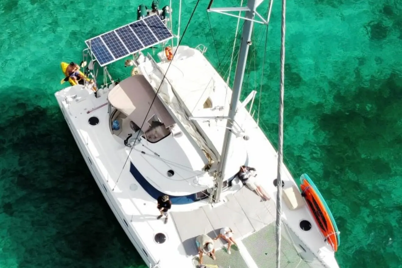 Overhead drone view of a sailing catamaran with solar panels anchored over green water near La Paz