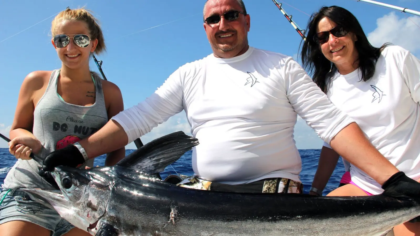 Man and two women holding a billfish across the gunwale of a sportfishing boat