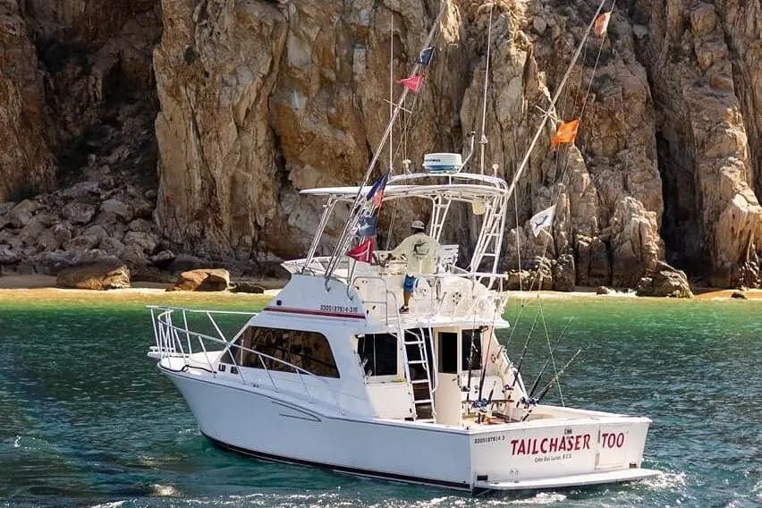 A flybridge sportfishing yacht flying fishing flags beside the granite cliffs of Cabo San Lucas