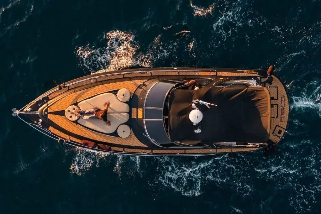 Overhead view of a person sunbathing on a motor yacht's bow on dark blue water off Cabo San Lucas at golden hour