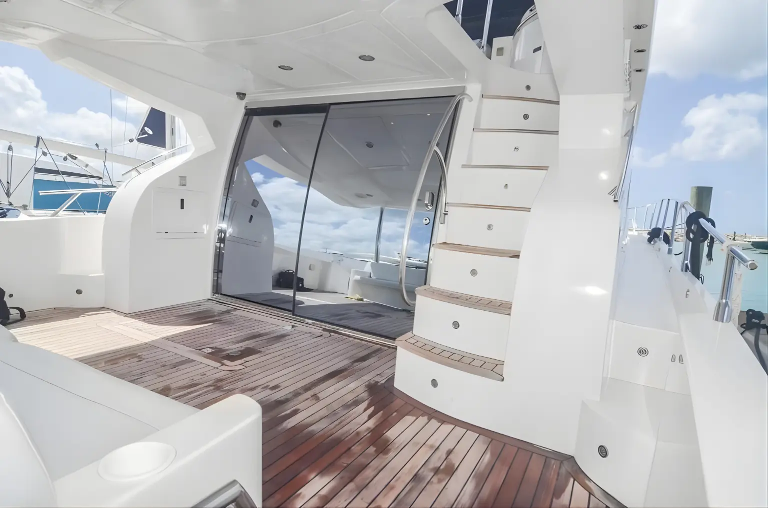 Teak aft deck of the yacht with glass doors to the salon and white stairs up to the flybridge