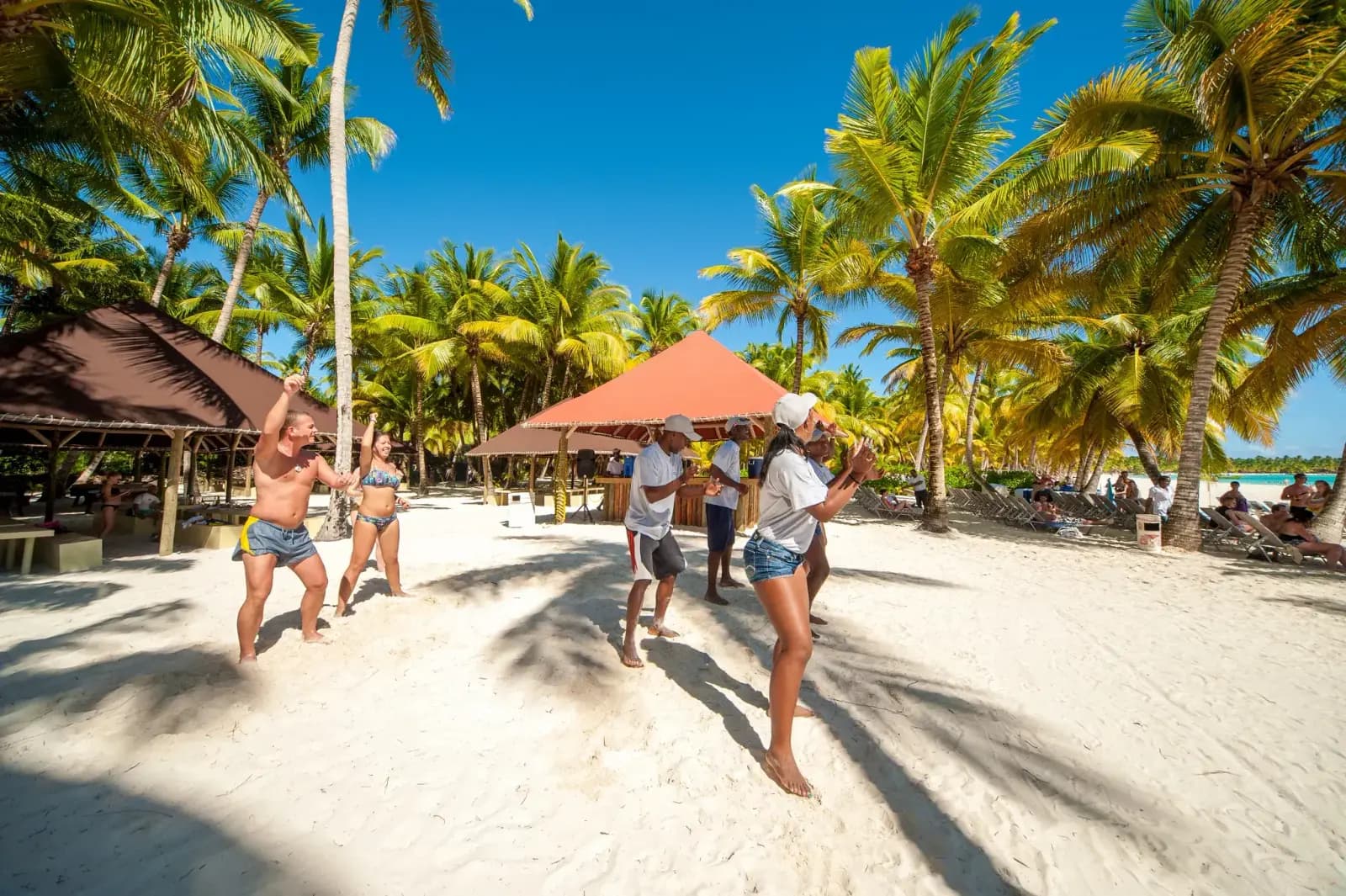Guests dancing on the palm-shaded sand beside beach huts on Saona Island