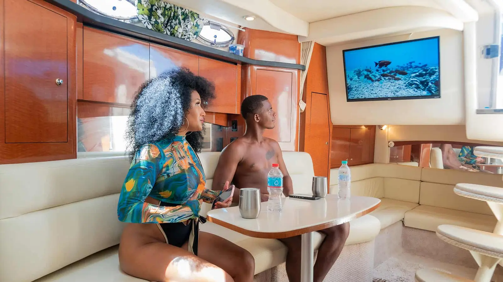 Woman and man chatting at the table in the yacht's wood-paneled cabin, TV on the wall
