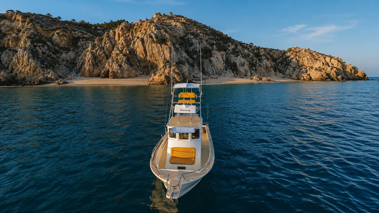 Aerial view of the sportfishing boat anchored off a sandy cove below rocky cliffs in Los Cabos