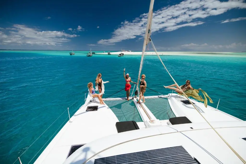 Guests lounging on the bow nets of a sailing catamaran over turquoise water off Zanzibar