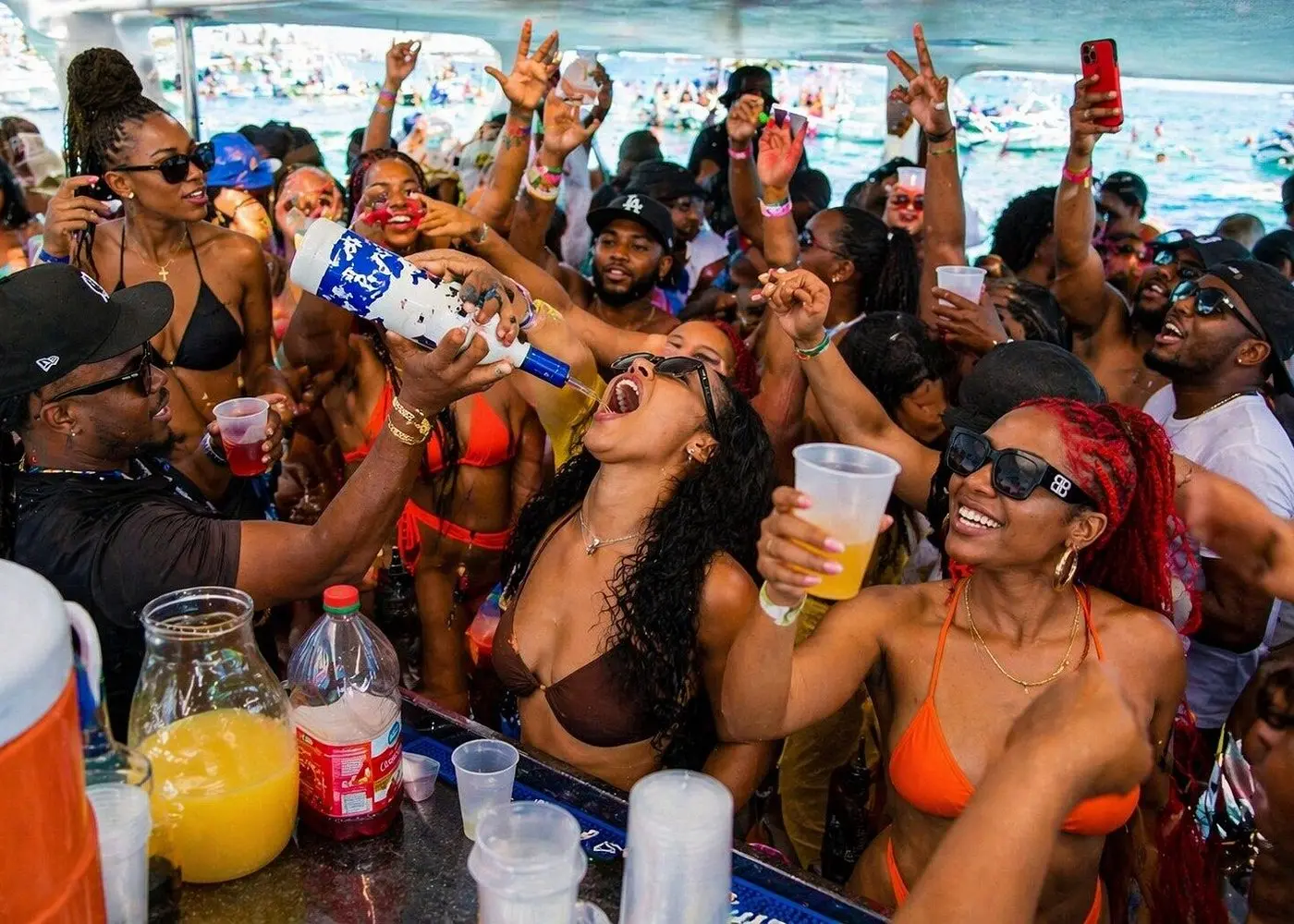 Man pouring a drink straight from the bottle into a woman's mouth at a packed deck party