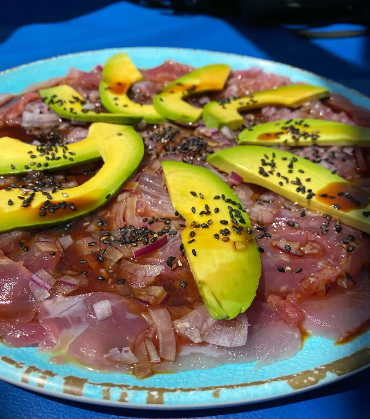 Plate of raw tuna with red onion, topped with sliced avocado and black sesame seeds
