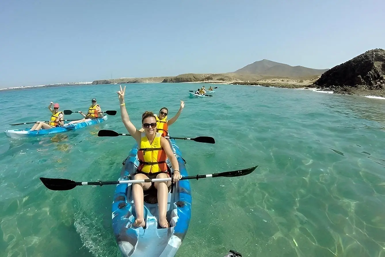 Guests in life vests paddling tandem kayaks through clear shallows along the desert coast near La Paz