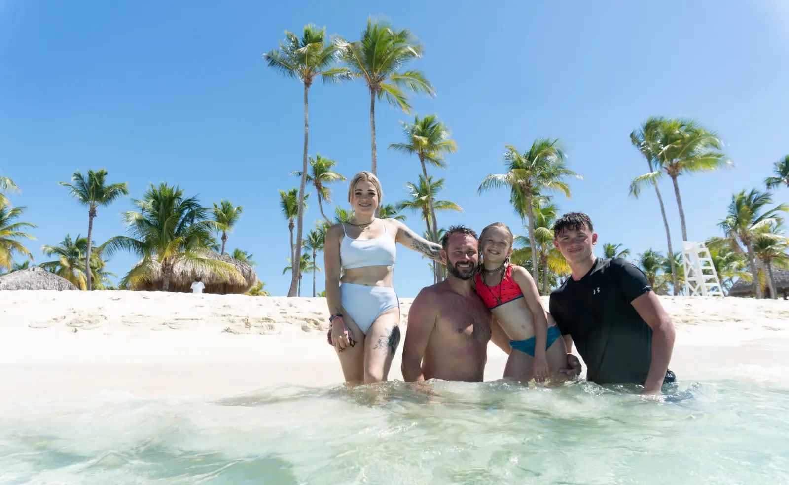 Family posing in clear shallow water in front of a palm-lined beach near Punta Cana