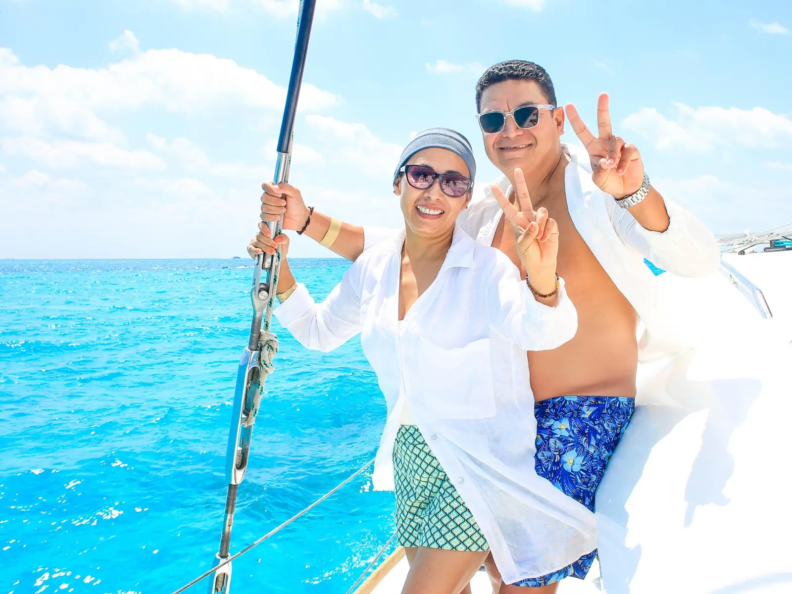 Couple flashing peace signs at the yacht's bow rail over bright turquoise water off Cancún