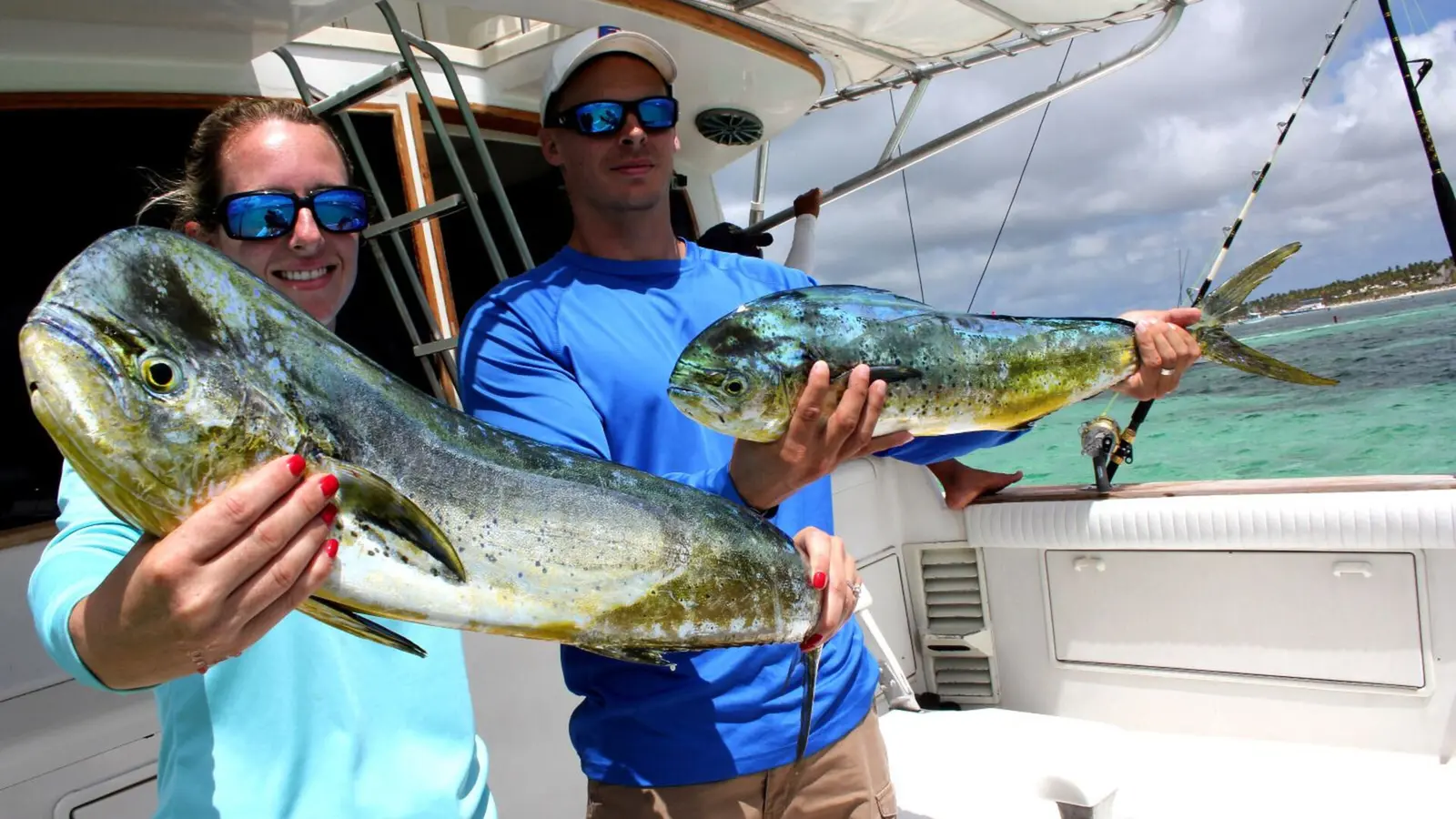 Woman and man each holding up a freshly caught mahi mahi on the fishing boat