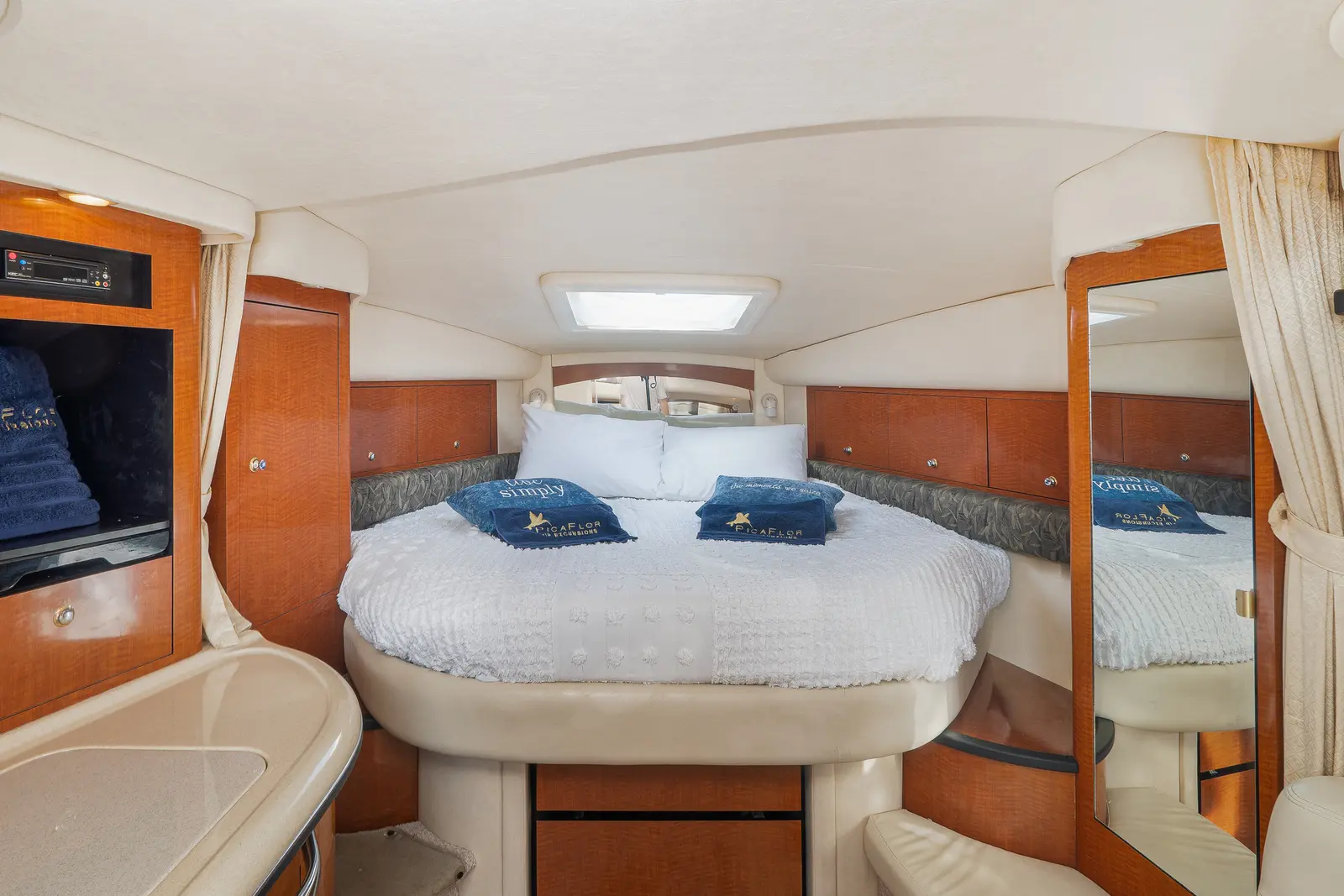 Forward cabin of the yacht with a double bed, white linens, navy pillows and cherry wood cabinets