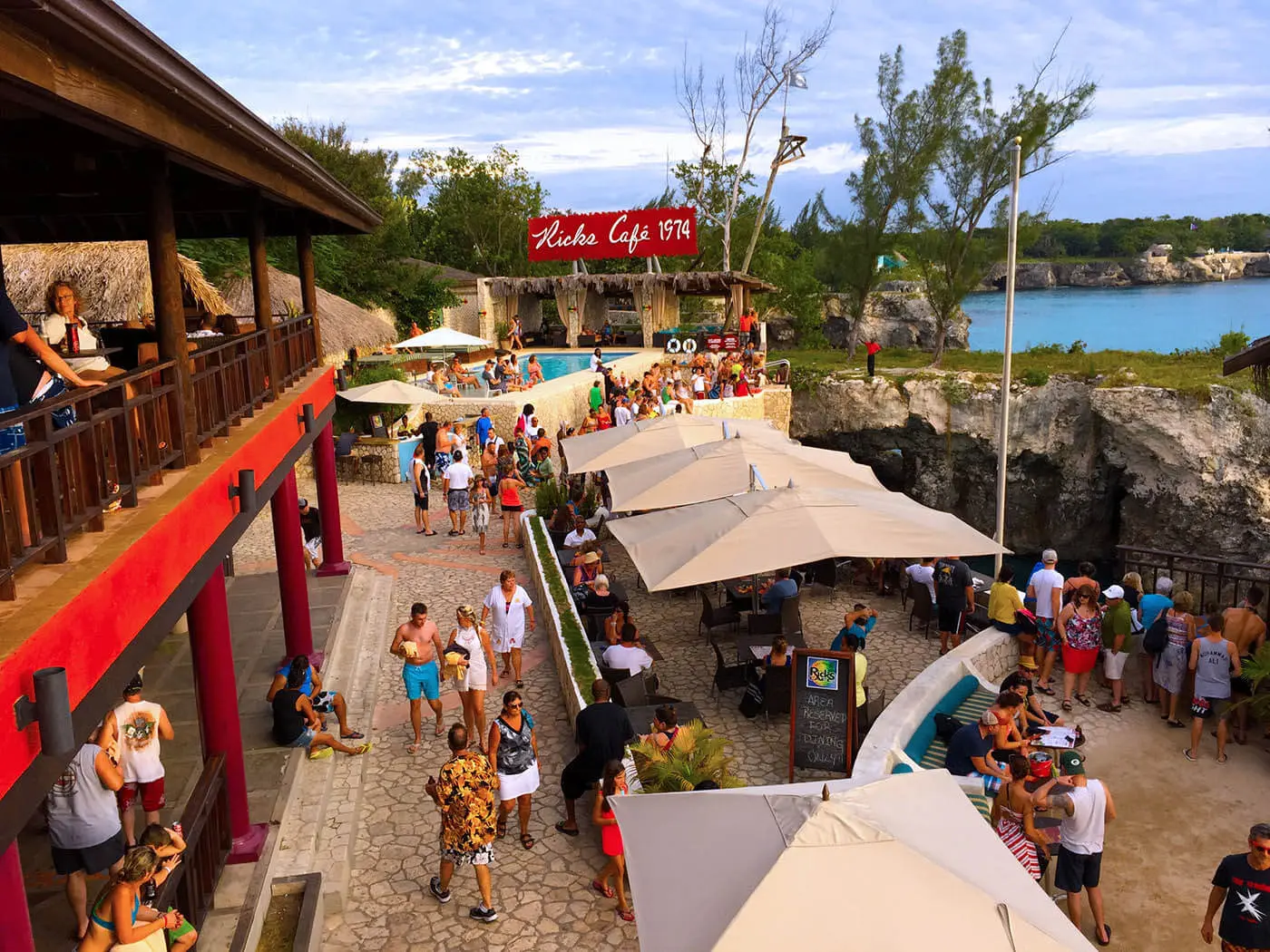 Crowds and white umbrellas on the clifftop grounds of Rick's Café above a turquoise cove