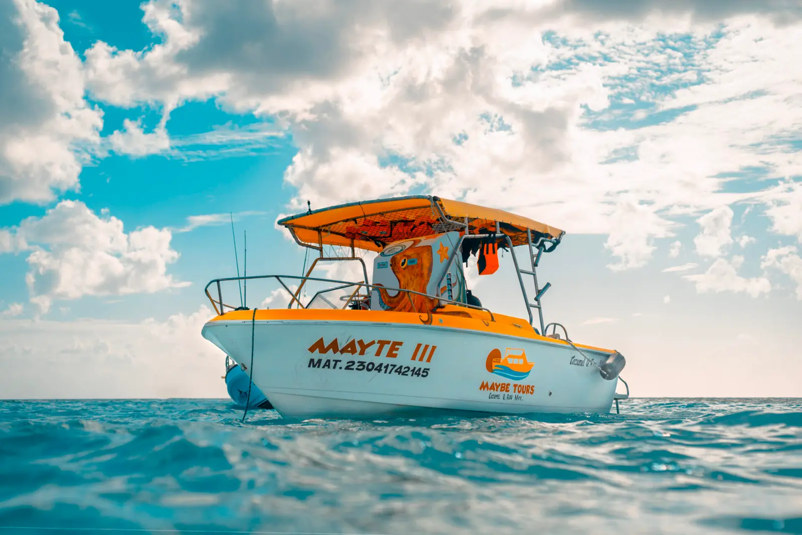 Speedboat with an orange canopy floating on turquoise water under puffy clouds in Cozumel