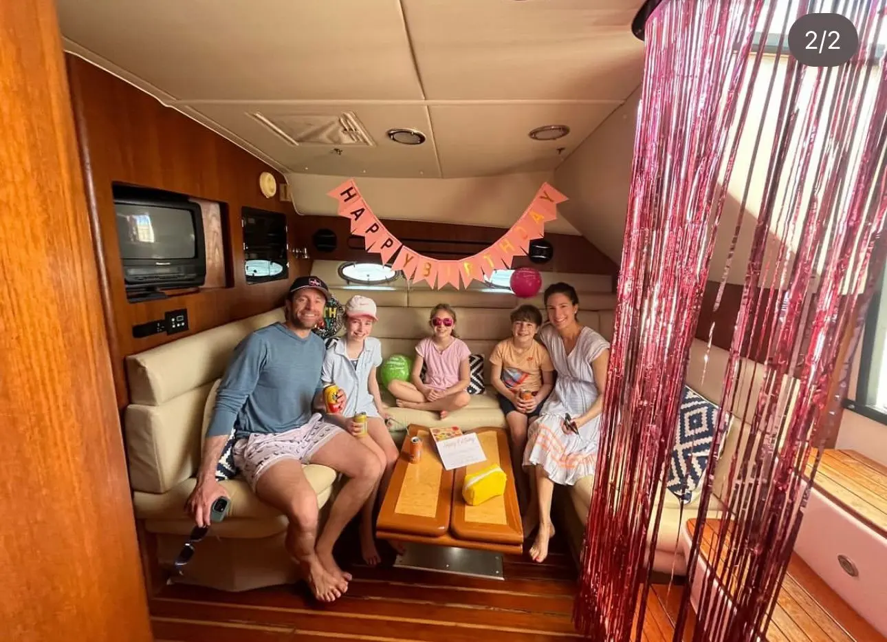 Family celebrating a birthday in the yacht's wood-paneled cabin with a pink banner and tinsel curtain