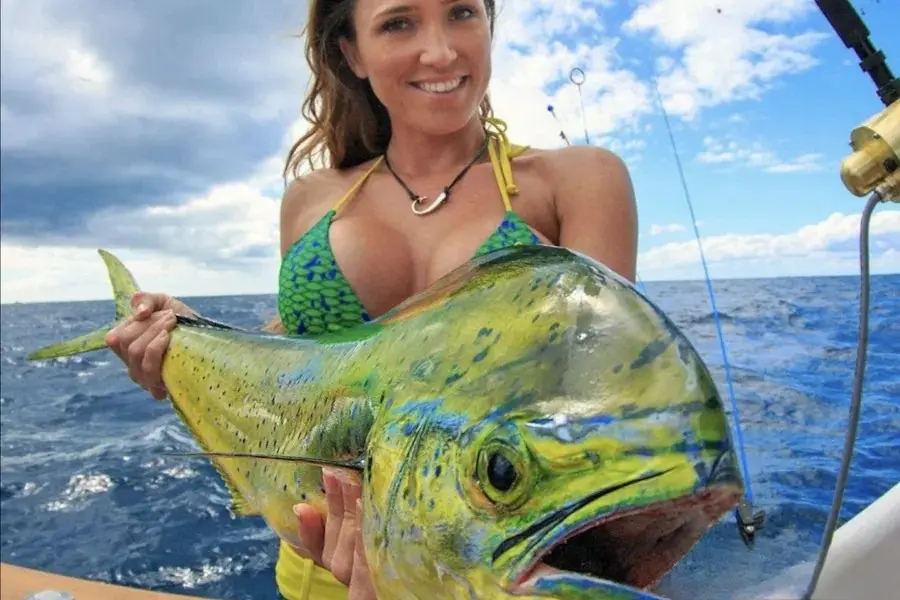Smiling woman holding a large green and yellow mahi-mahi on a sportfishing boat at sea