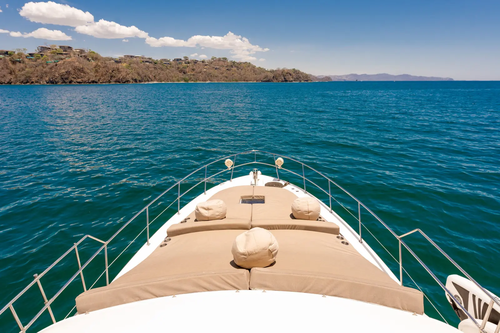 View from the motor yacht's cushioned bow sunpad toward the dry forested coast of Papagayo