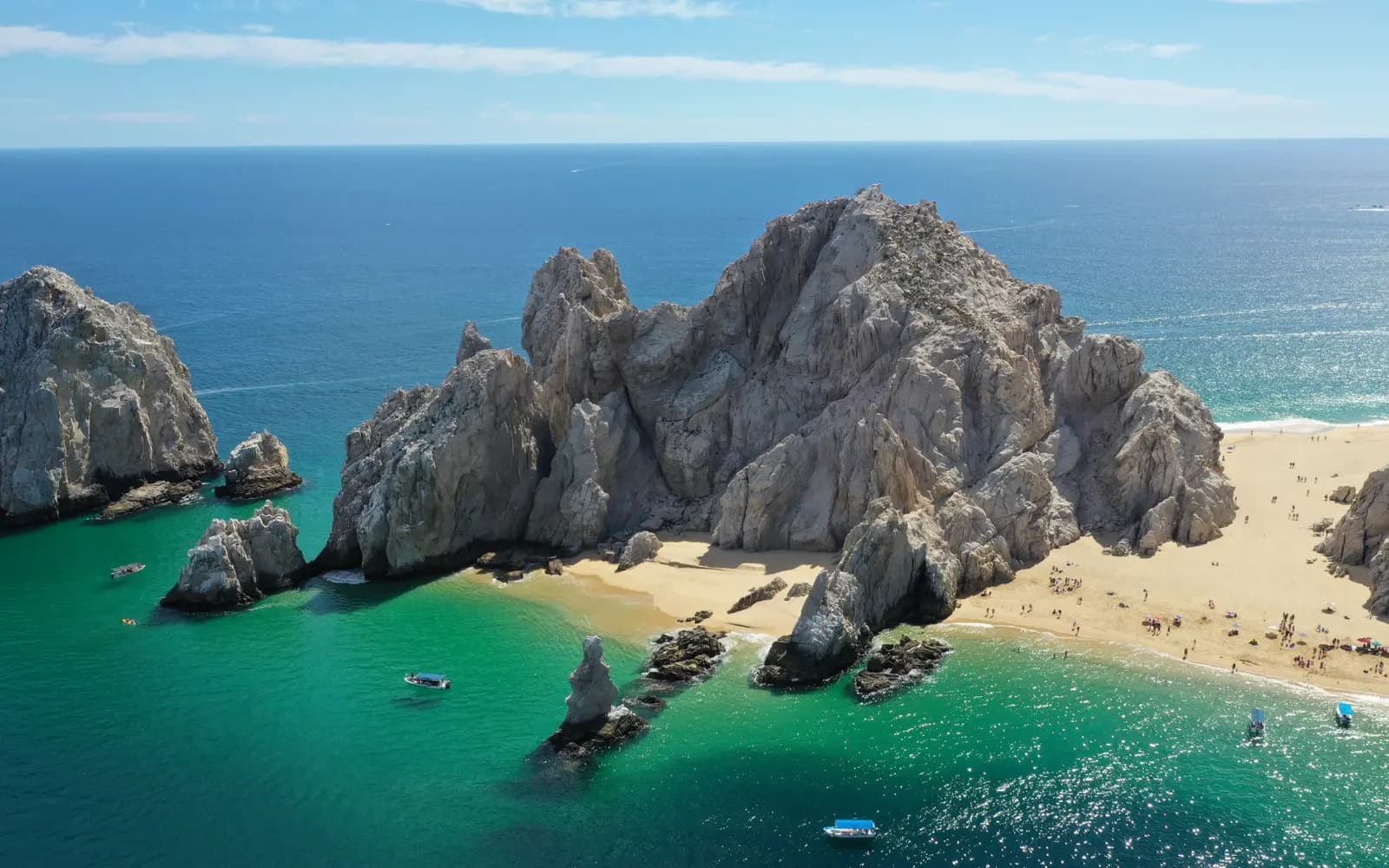 Aerial view of the Land's End headland with beaches on both sides and boats in green water