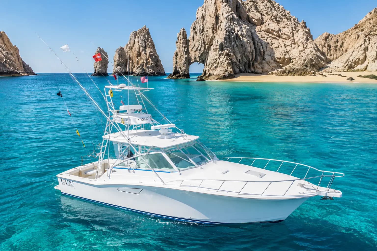 Sportfishing yacht with a tuna tower anchored in turquoise water beneath the rock formations of Los Cabos