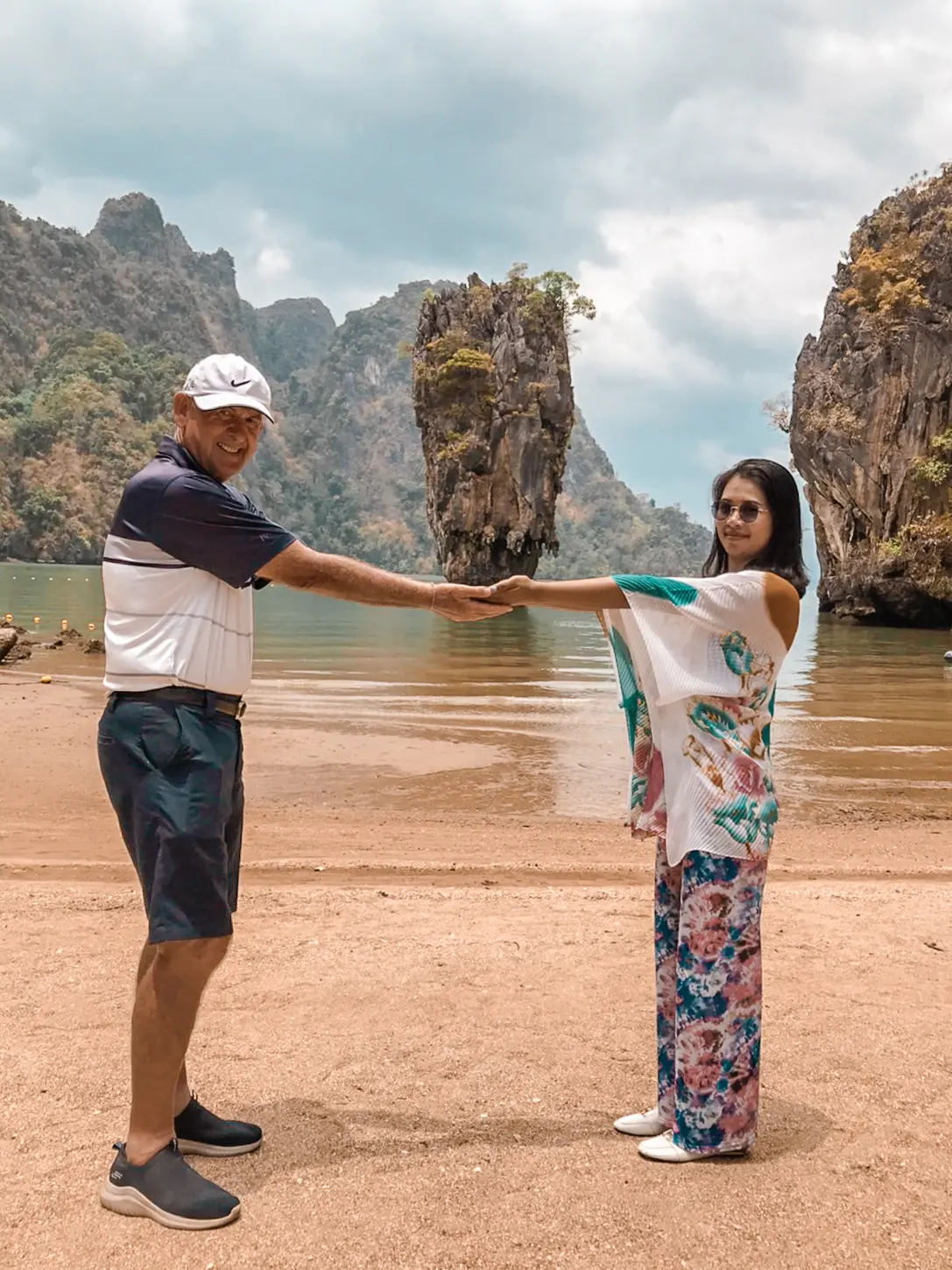 Couple holding hands at arm's length on the sand with James Bond Island's needle rock behind
