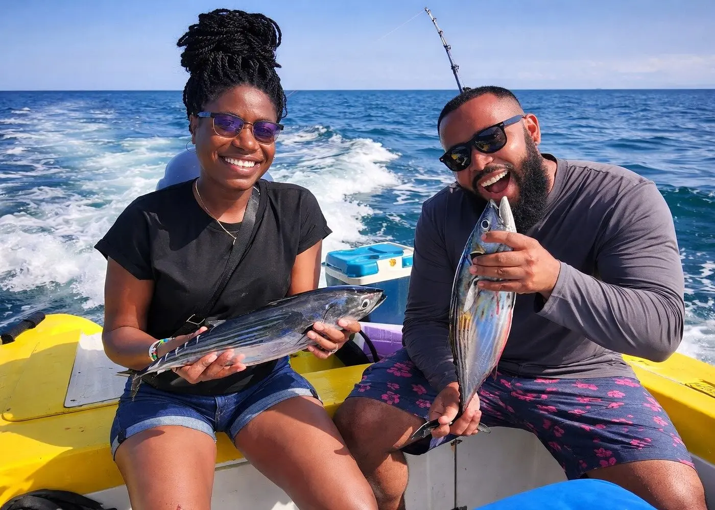 A woman and a man laugh at the stern of the yellow panga, each holding up a small tuna