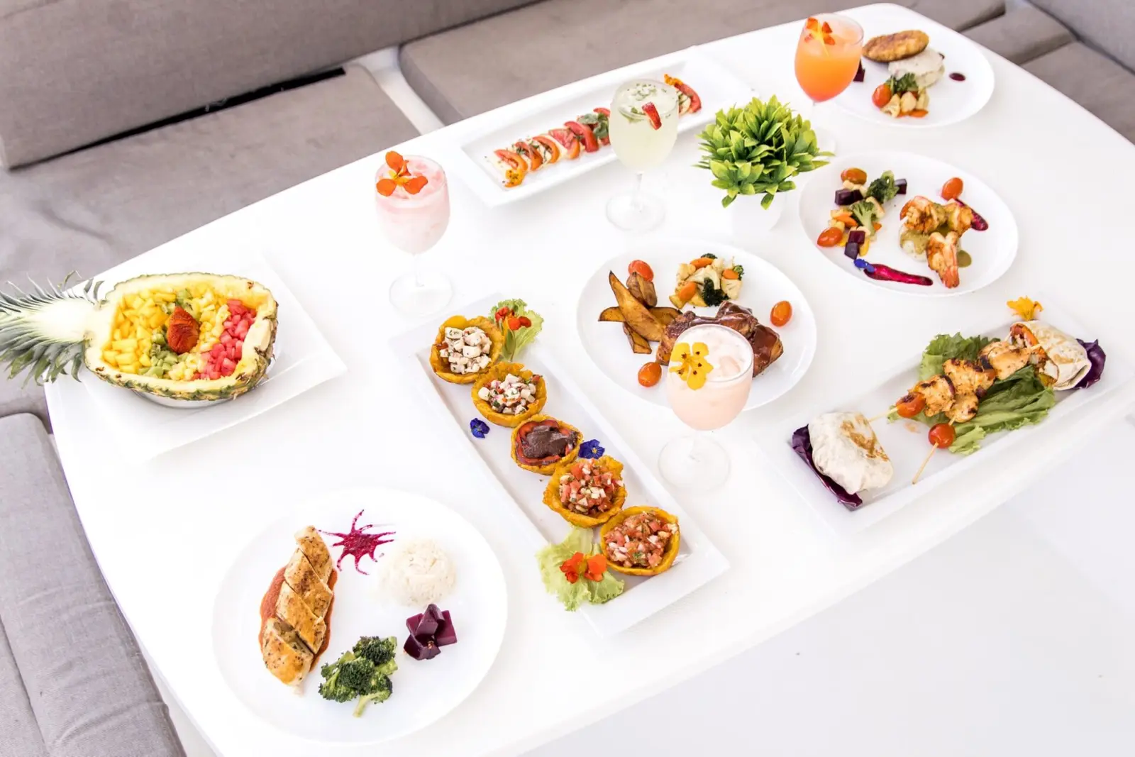Plated appetizers, sushi rolls, a pineapple fruit boat and cocktails on the catamaran's white table