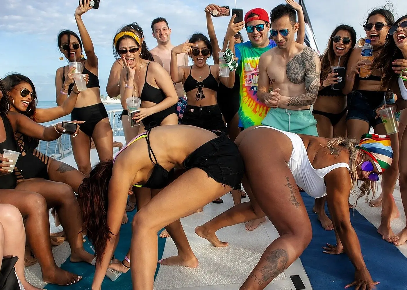 Women dancing on the catamaran deck as guests cheer and film with phones