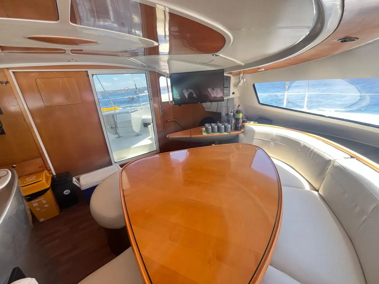 Wide view of the yacht saloon with a curved cream sofa, varnished table and flat-screen TV