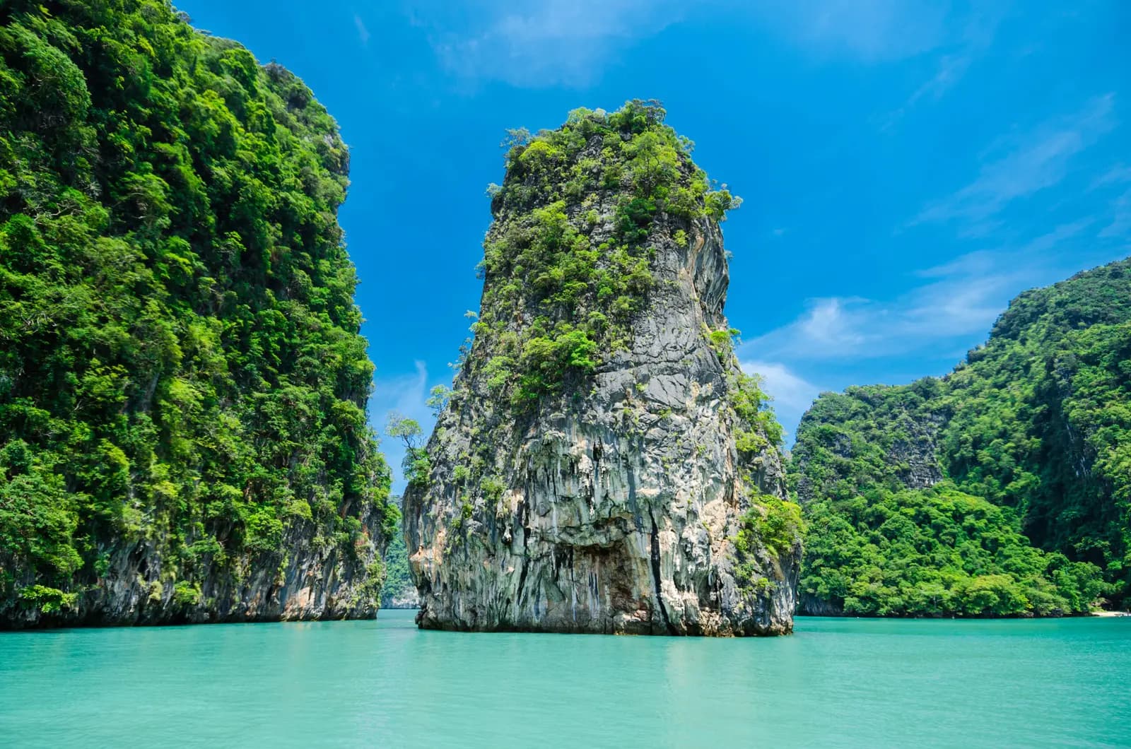 Jungle-topped limestone pillar standing in turquoise water between green karst cliffs in Phang Nga Bay