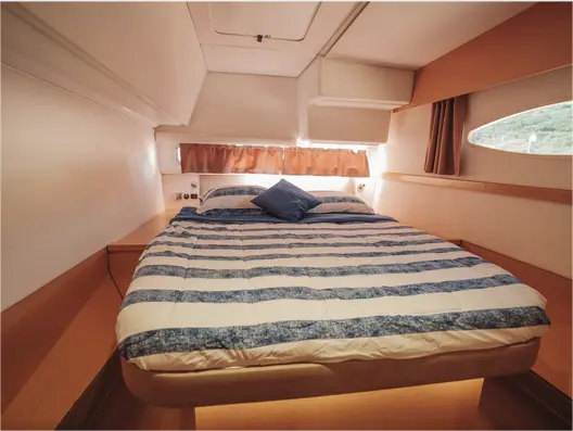 Double cabin with blue-and-white striped bedding and a hull porthole on the sailing catamaran