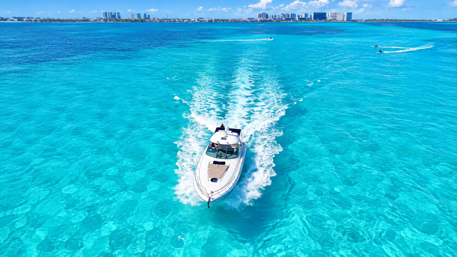 Motor yacht speeding across turquoise water with the Cancún hotel zone skyline in the distance