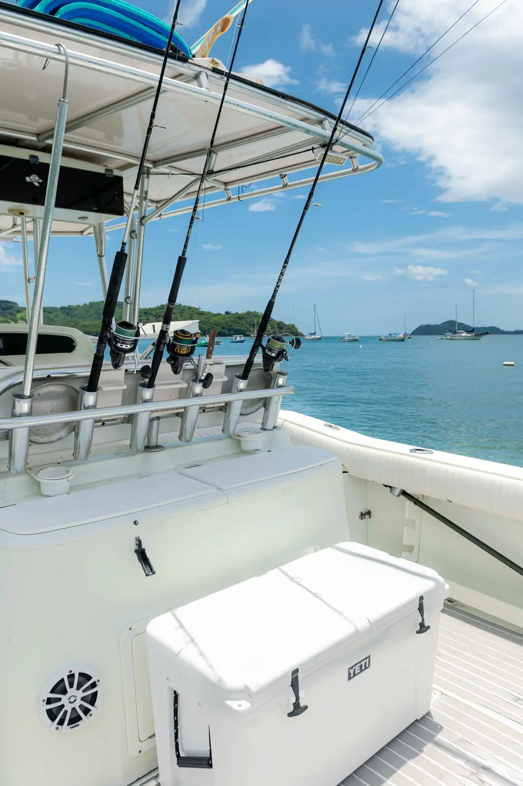White cooler on deck below fishing rods racked on the T-top of a center console boat in a calm bay
