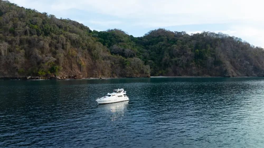 Motor yacht anchored alone in a calm bay beneath forested hills in Costa Rica