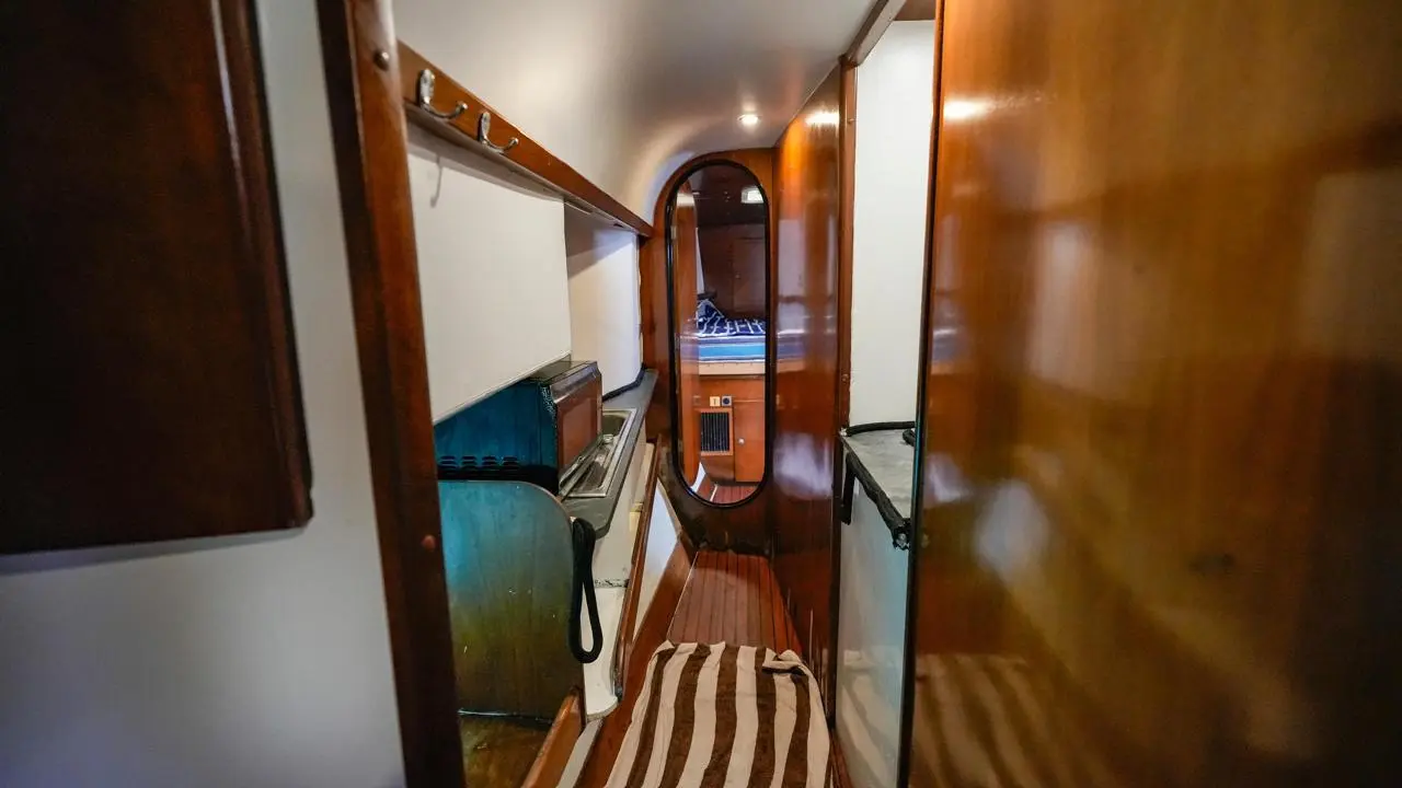 Narrow wood-panelled corridor inside a catamaran hull leading to a cabin with a striped berth