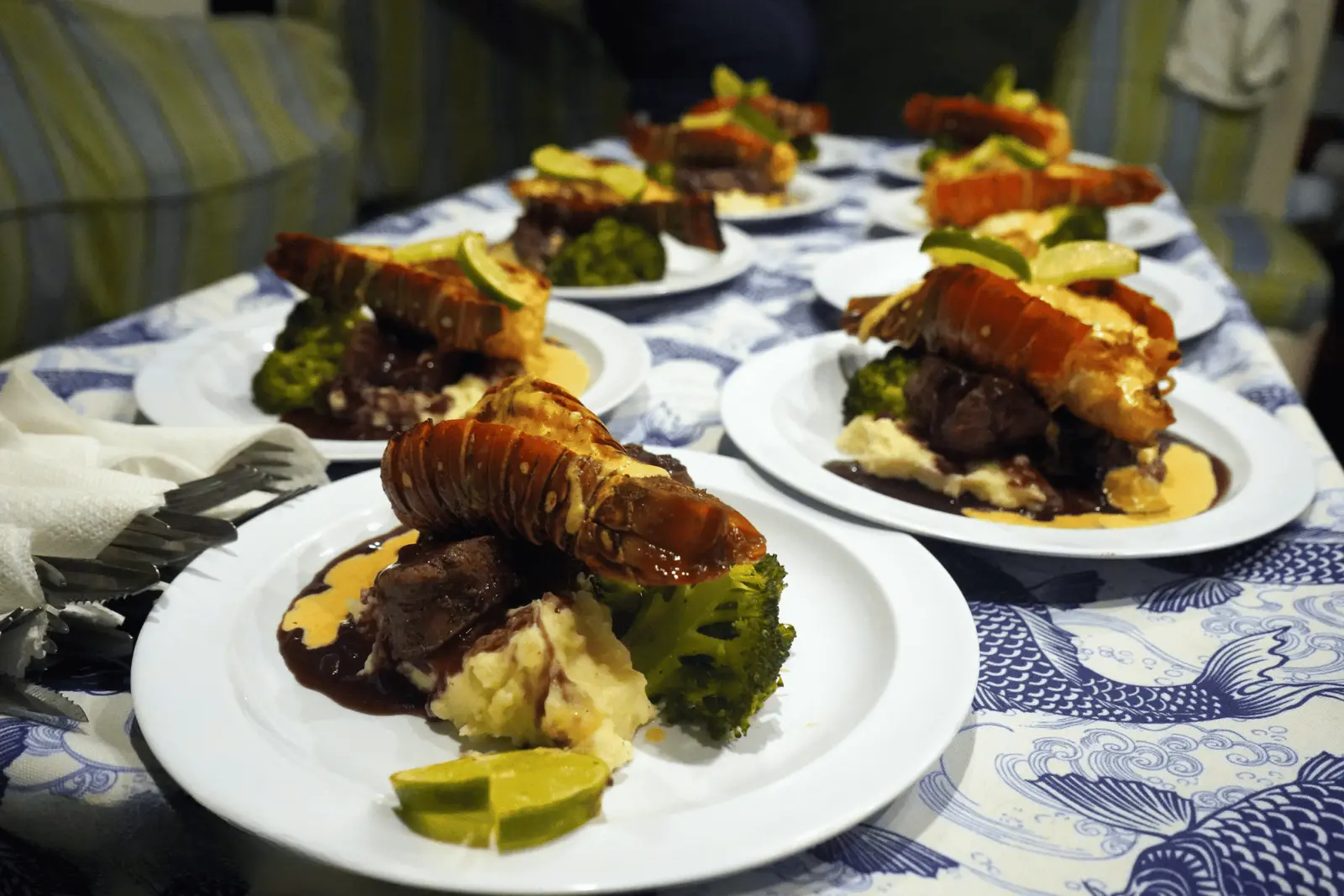 Plated surf and turf of lobster tail and steak with mashed potatoes, broccoli and lime wedges