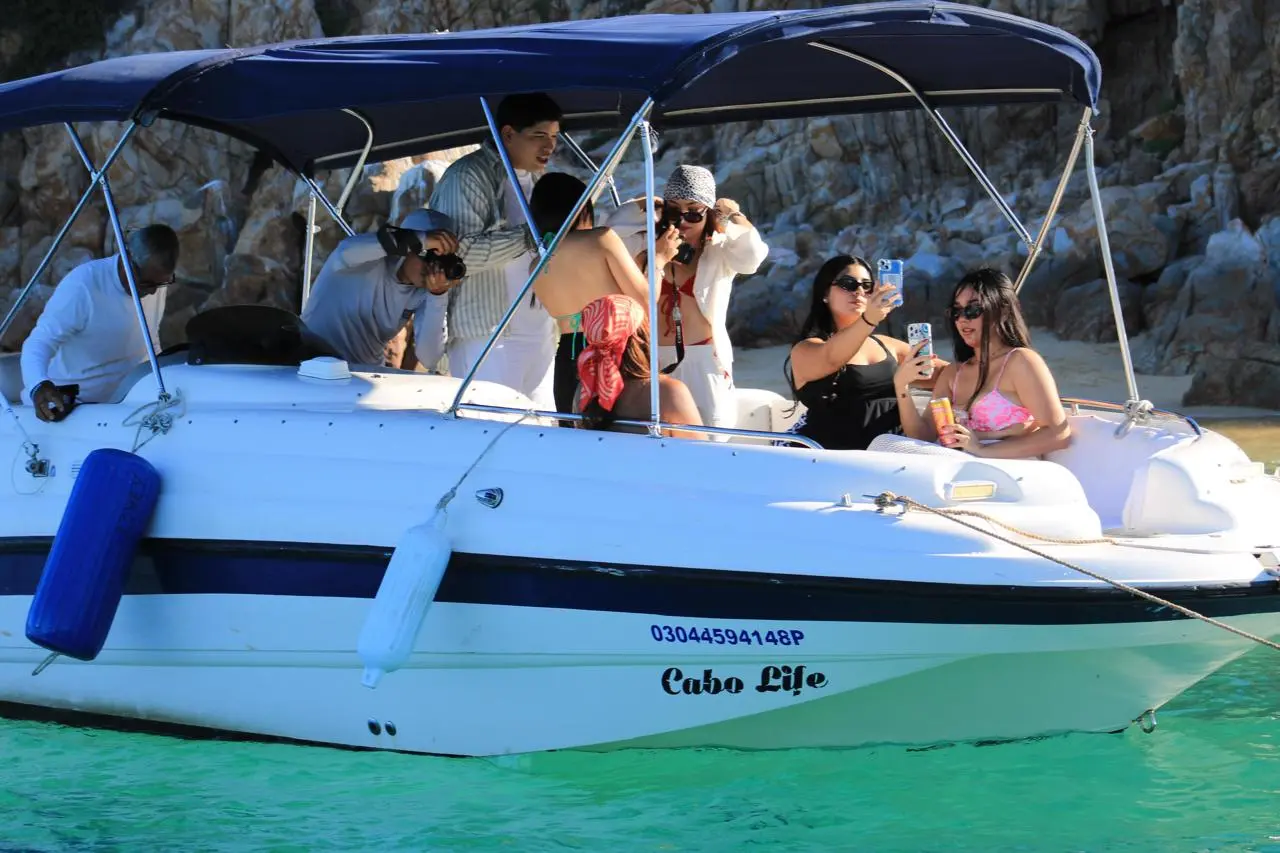 Women taking selfies on a yacht's padded seats as friends chat under the canopy in a Cabo San Lucas cove