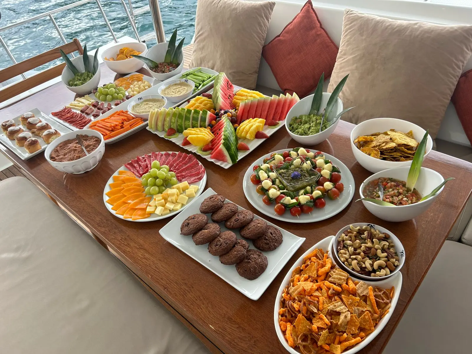 Snack spread of fruit, cheese, cured meats, cookies, nuts and chips on a sailing catamaran table