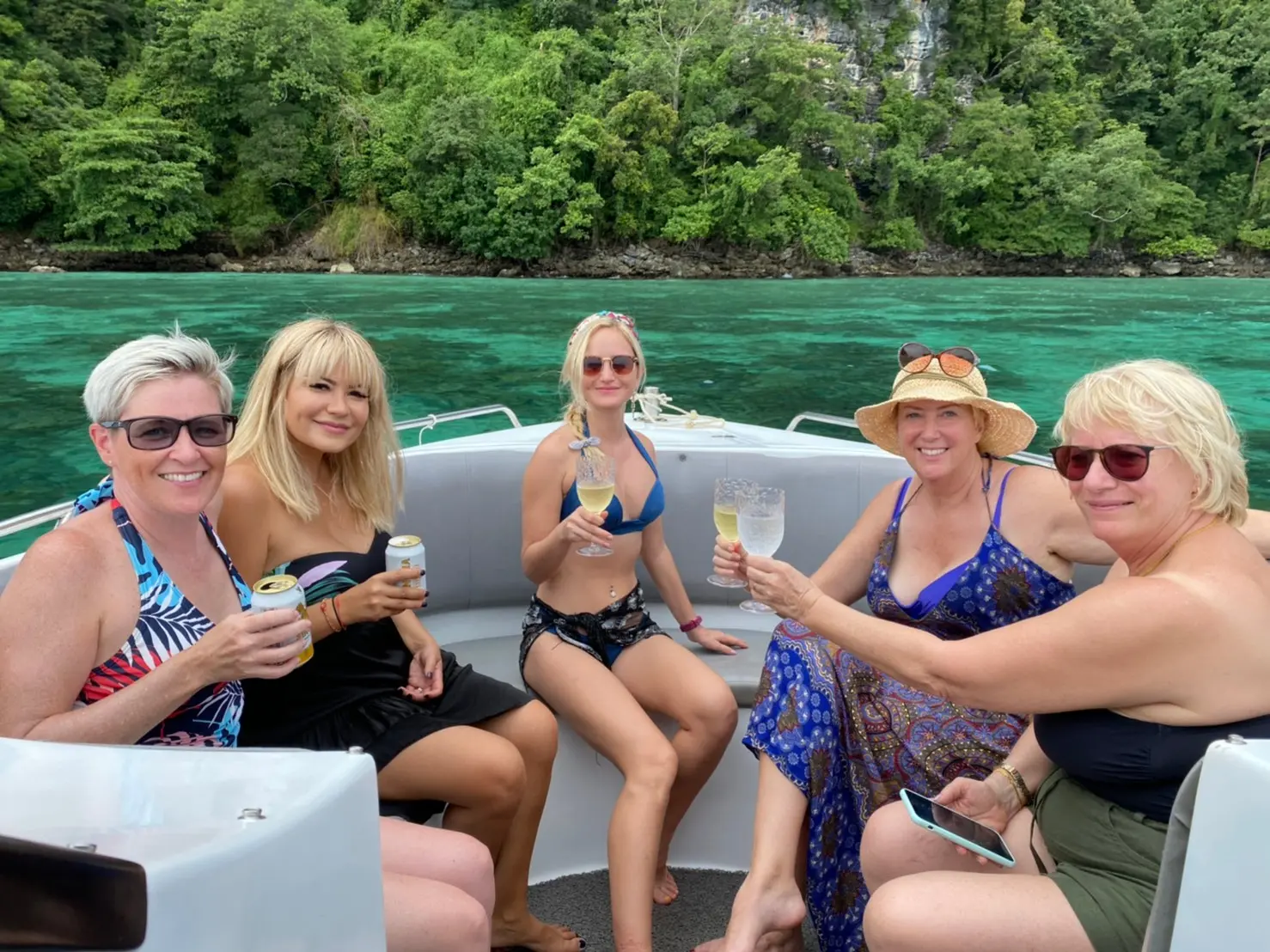 Five women raising drinks on the speedboat's cushioned seats off a jungle-covered island in the Andaman Sea