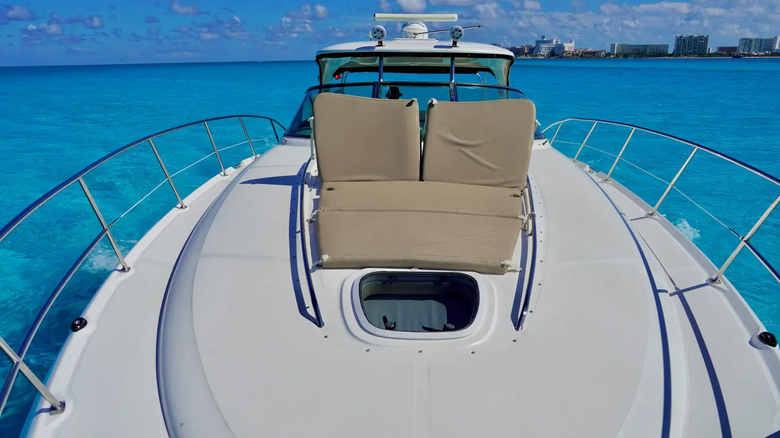 Foredeck of a motor yacht with beige cushioned seating and steel rails on the open sea off Cancún