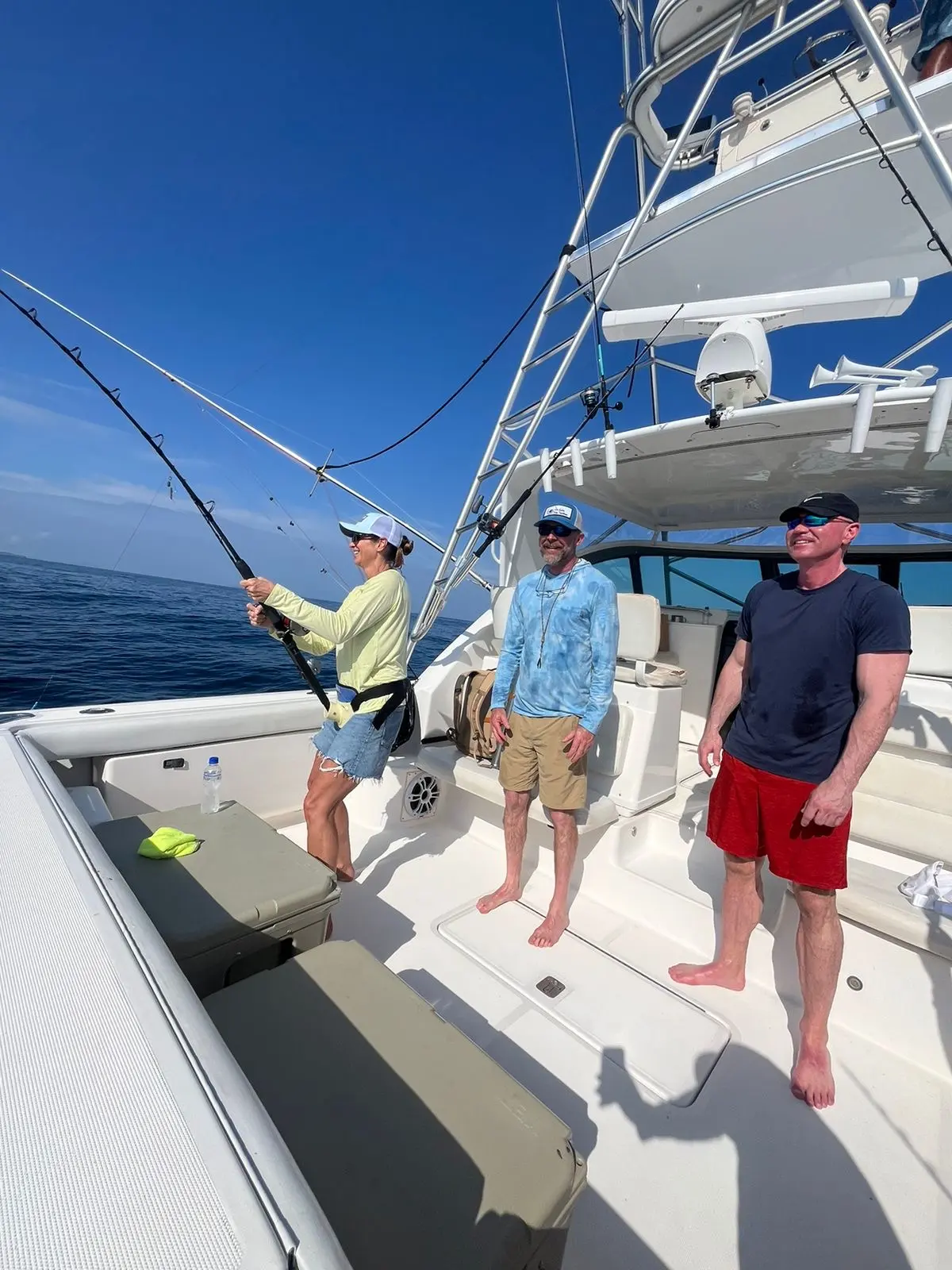 Three men in the cockpit of the sportfishing yacht as one works a bent rod under the tower
