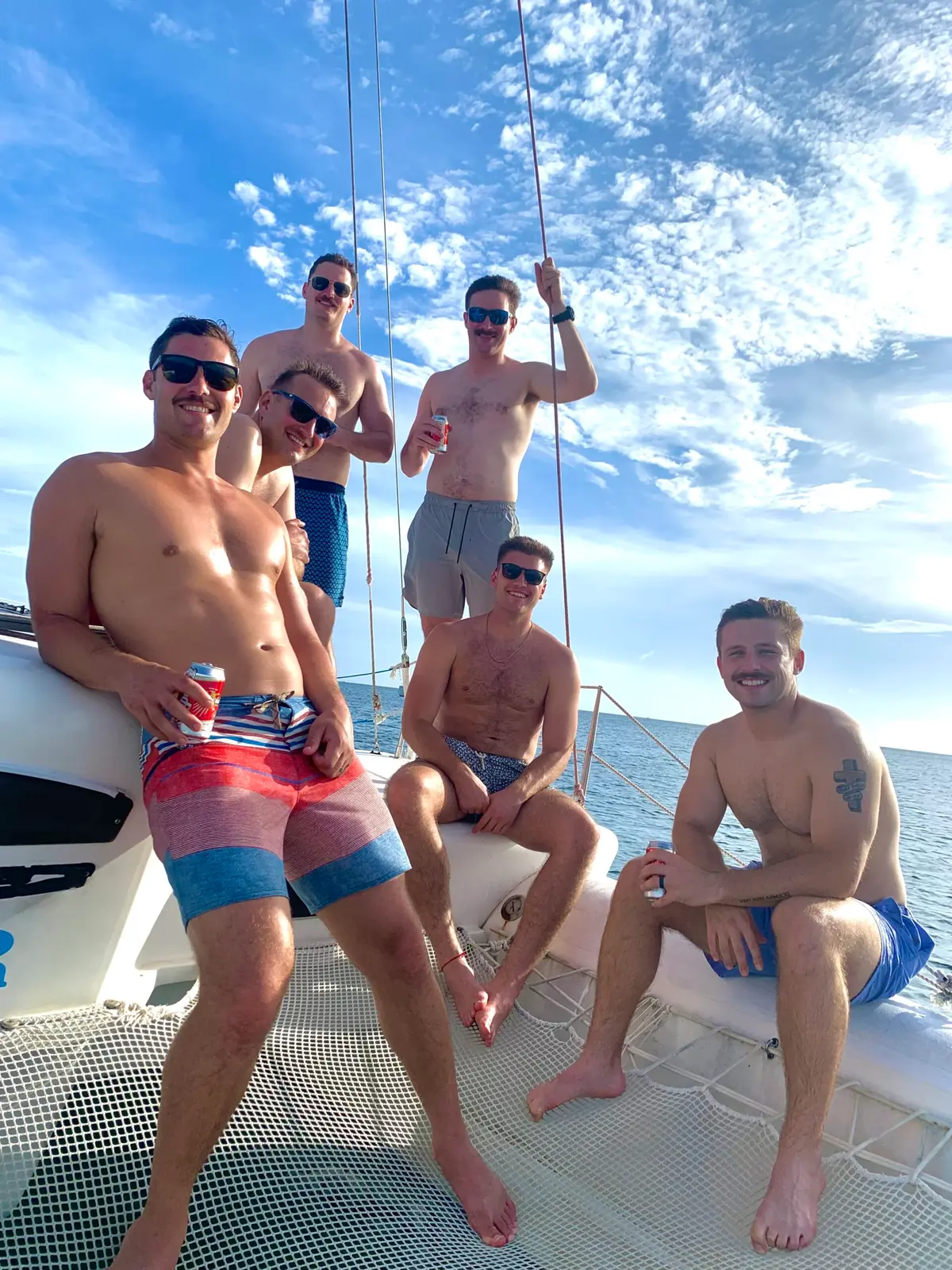 Five men in swim trunks posing on the sailing catamaran's trampoline under a blue sky