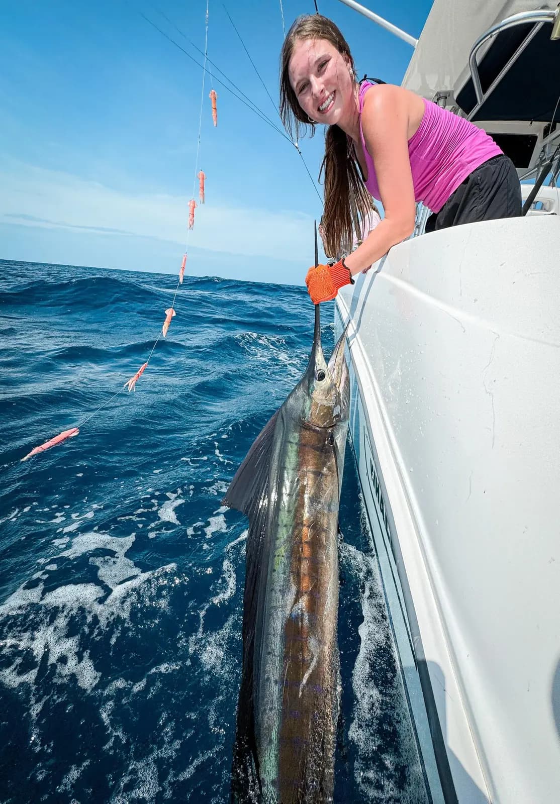 Angler in a pink top leaning over the gunwale to bring a hooked fish alongside the boat in open water