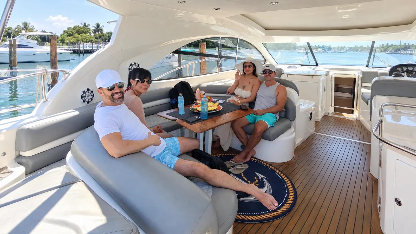 Two couples relaxing around a table in the cockpit lounge of a sport yacht docked at a marina