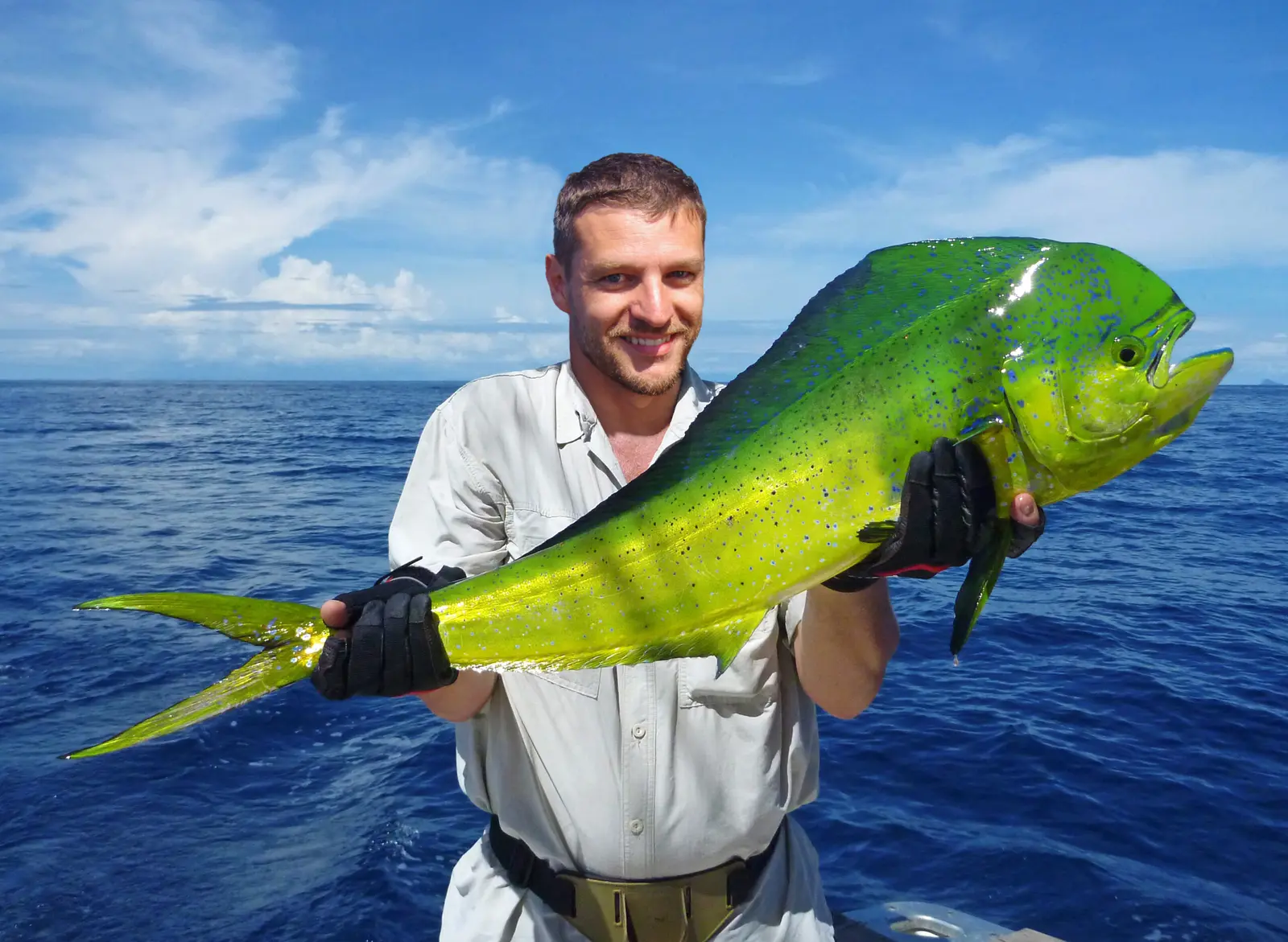 Angler in fishing gloves showing off a bright green and gold mahi-mahi under a blue sky