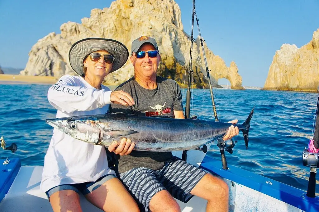 A couple with a freshly caught wahoo on a fishing boat by the Cabo San Lucas arch