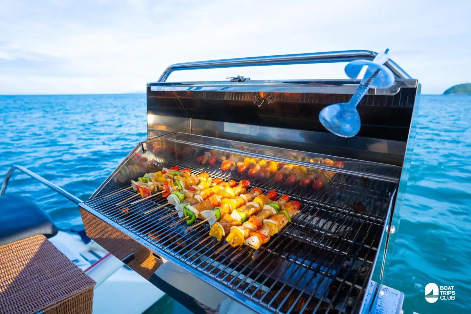 Meat and vegetable skewers sizzling on a stainless steel grill aboard a catamaran, open sea behind