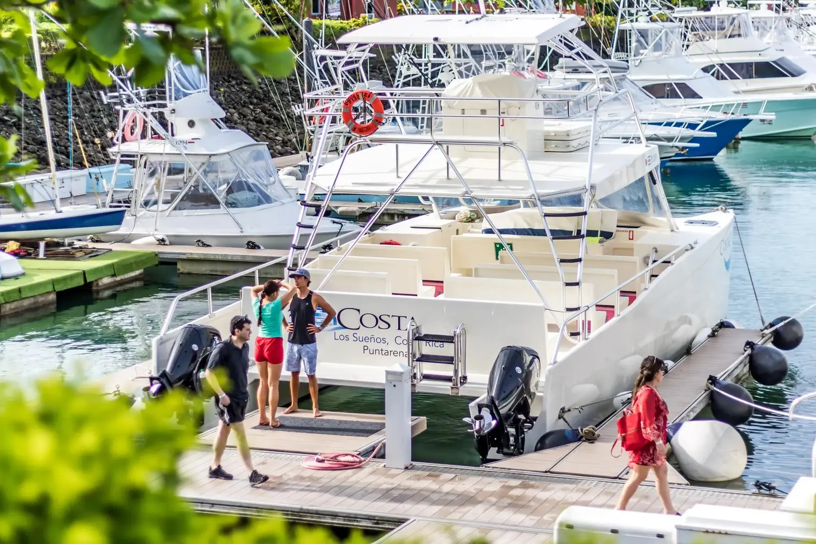 Guests walking the dock beside the catamaran at Los Sueños Marina, sportfishing boats moored behind